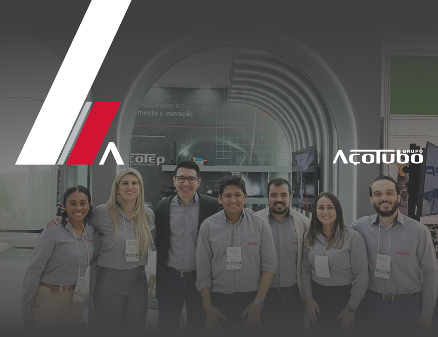 alt="sete colaboradores do Grupo Açotubo reunidos lado a lado em frente a um estande"