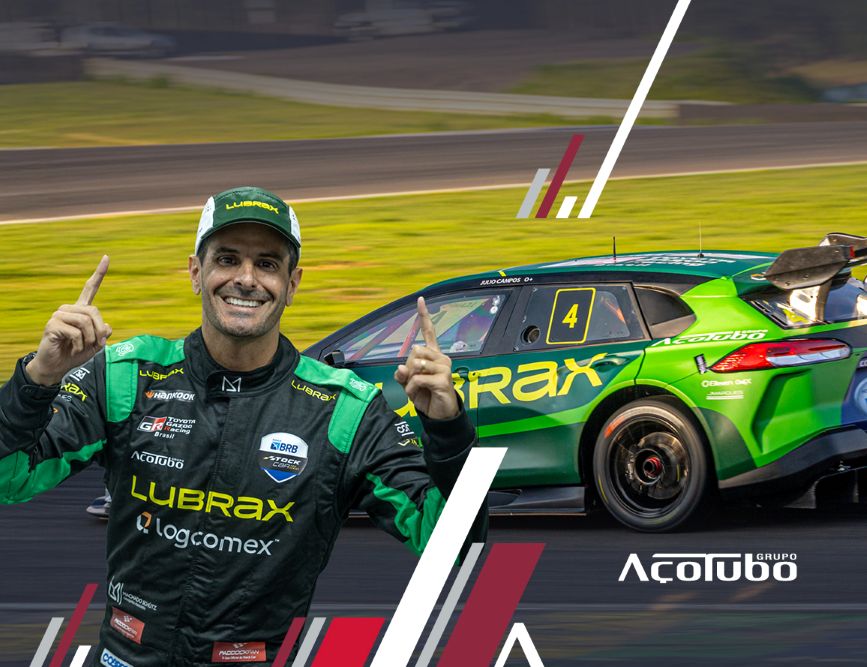alt="Julio Campos, piloto da Stock Car, com o seu uniforme ao lado do carro branco e vermelho com o logo da parceira Açotubo"